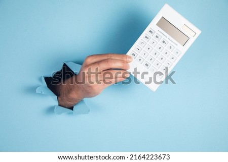 A man hand holds a calculator on blue background.