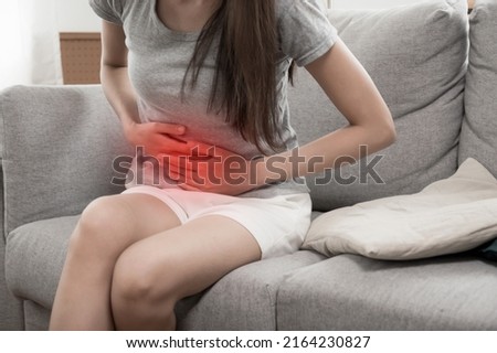 asian young woman suffering stomach ache sitting on couch in living room at home, people painful stomachache, gynecology, menstrual pain , medical and health care concept Royalty-Free Stock Photo #2164230827