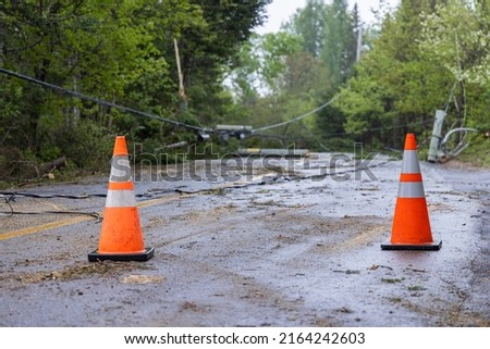 Two traffic cones are used to warn traffic of road closure due to uprooted trees and dangerous overhead power cables lying in road after high winds. Royalty-Free Stock Photo #2164242603