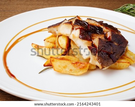 Baked cod, halibut, fillet of white fish. Fish with baked potato slices with lemon and rosemary herbs sauce on a white plate. Serving dishes in the restaurant. Lunch, dinner. Photos for the menu.