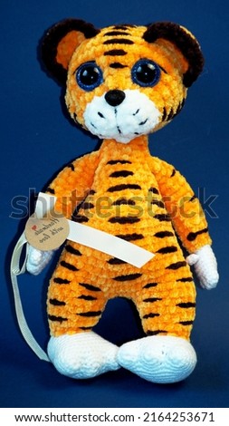 a knitted tiger toy stands on a blue background.  handmade work. gift. a handmade stuffed toy. side view. handmade work