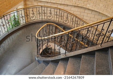 spiral staircase in the interior with marble floor and elegant wrought iron balusters with wooden railings Royalty-Free Stock Photo #2164267809