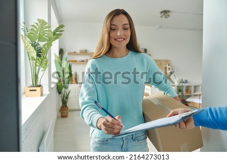Happy young woman accepting box from delivery man and signing paper