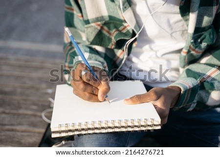 Closeup of artist hand drawing sitting outdoors, selective focus. Writer taking notes into paper notepad   
