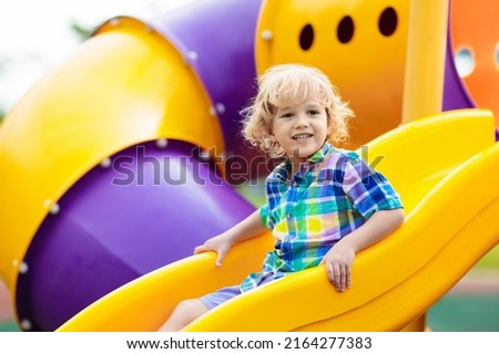 Child playing on outdoor playground. Kids play on school or kindergarten yard. Active kid on colorful slide and swing. Healthy summer activity for children. Little boy climbing outdoors. Royalty-Free Stock Photo #2164277383