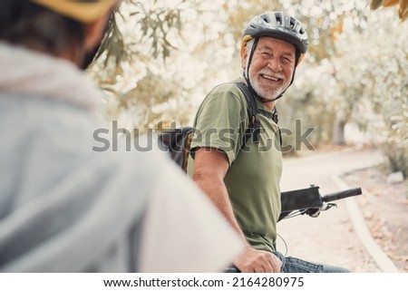 Two happy old mature people enjoying and riding bikes together to be fit and healthy outdoors. Active seniors having fun training in nature. Portrait of one old man smiling in a bike trip with wife Royalty-Free Stock Photo #2164280975