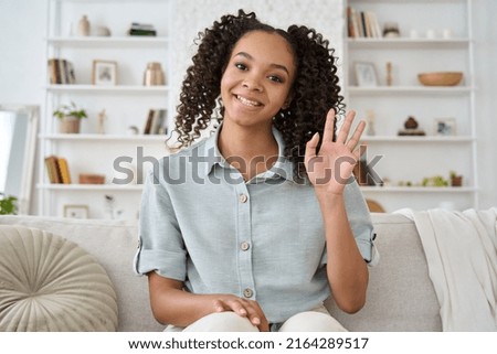 Happy African American teen girl blogger smiling face waving hand talking to webcam recording vlog, making video call at home. Distance video communication or vlogging concept. Webcamera view Royalty-Free Stock Photo #2164289517
