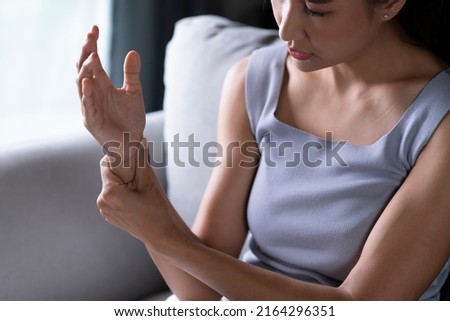 Young Asian woman wearing casual clothes suffering pain on hands and fingers, arthritis inflammation. Woman has pain in wrist. Health care and medical concept.