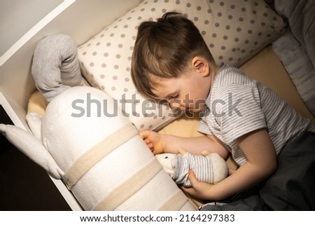 A little cute boy in stylish pajamas falls asleep in his bed in the children's room. With your favorite mouse toy. Preparation for sleep. The child falls asleep on his own.