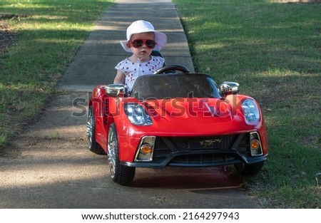 Caucasian baby in white hat riding in an electric convertible red sport car. child driving car on a summer day Royalty-Free Stock Photo #2164297943