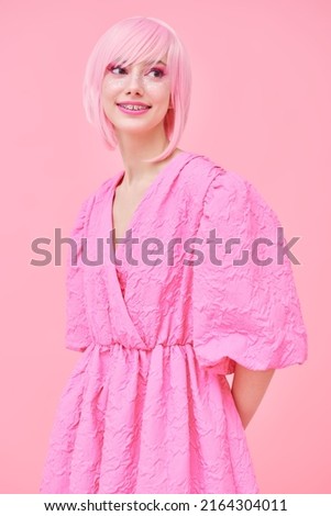 Beauty, fashion. Portrait of a cute teen girl with bright pink makeup and pink hair smiling and posing in fashionable pink dress. Pink background.