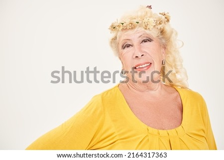 Studio portrait of a romantic senior woman in her 80s wearing a flower wreath smiling at the camera. Fashion and beauty of the elderly. Studio portrait.