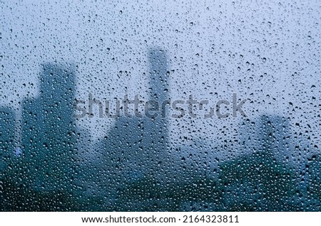 Rain drop on glass window at day time in monsoon season with blurred city buildings background. Royalty-Free Stock Photo #2164323811