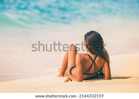 Beach woman lying down on sand relaxing sunbathing on Caribbean travel summer vacation lifestyle. View from behind girl tanning under the sun in black bikini Royalty-Free Stock Photo #2164332519