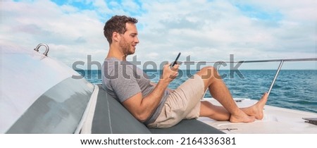Phone using on cruise ship. Man luxury travel texting with data on yacht boat relaxing on deck banner panoramic. Caribbean vacation Royalty-Free Stock Photo #2164336381
