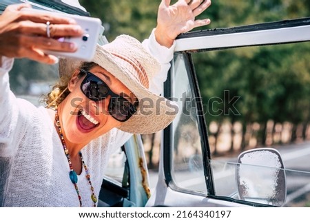 Overjoyed and excited young woman taking selfie picture with mobile smartphone. Female people use cellular during travel. Road and outdoors in background. People sharing life on social media