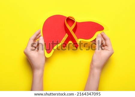 Woman with awareness ribbon and paper liver on yellow background. Hepatitis concept