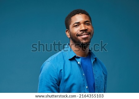 Portrait of smiling African American man wearing blue on blue background and looking at camera, copy space