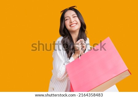 Asian happy female woman girl holds colourful shopping packages   standing on yellow background studio shot, Close up Portrait young beautiful attractive girl smiling looking at camera with bags Royalty-Free Stock Photo #2164358483