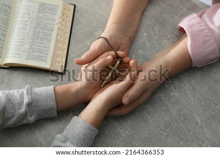 Boy and his godparent holding cross at grey table, closeup