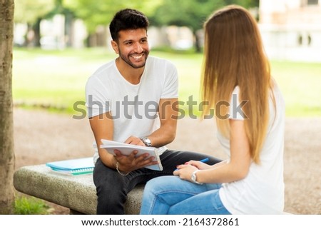 Two students studying together sitting on a bench outdoor