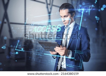 Attractive young european businessman using tablet in blurry office interior with access hologram. Technology and data concept. Double exposure