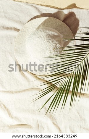 Summer minimal background, top view wide-brimmed sun hat under palm leaf on beach towel on sand. Summer aesthetic photography pastel beige colored, copy space, vacation, relaxation concept. Vertical