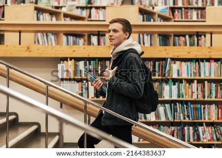 Young male student going up the stairs in library. Man with textbooks in university library.