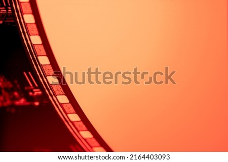 Part of vintage filmstrip in soft red light. Analog old strips of film for a photo or video camera close up. Selective focus on film perforation. The concept of cinematography, photography.