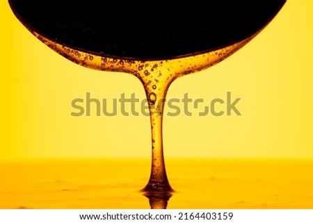 Honey dripping, pouring from dark spoon on yellow background. Thick viscous honey molasses flowing. Close up of golden honey liquid, sweet product of beekeeping. Sugar syrup is pouring.