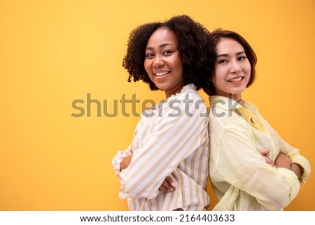 Young beautiful african american girl with an afro hairstyle and friends with positive thinking. Attractive girl wearing shirt and bright smiling. Portrait on yellow background.