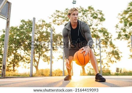Young cool sunlit concentrated sporty sportsman man wear sports clothes doing handling drills training holding in hand ball play at basketball game playground court Outdoor courtyard sport concept.