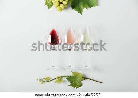 Flat-lay of red, rose and white wine in glasses and Branch of vine leaves on white background. Wine bar, winery, wine degustation concept. Minimalistic trendy photography Royalty-Free Stock Photo #2164452531