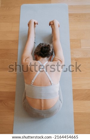 Top view photo of senior healthy lady sitting on floor on the yoga mat and doing splits in white light domestic room. Stock photo