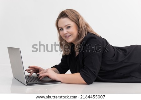 Smiling and contemplating blond woman lying on floor, using laptop for job, white background. Working on her new article