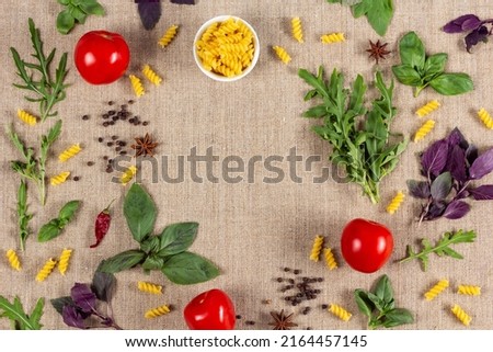 Fresh herbs, spices and vegetables with italian raw pasta on linen cloth background and copy space in the center.