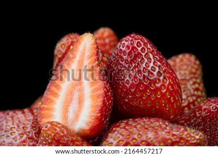 Close-up of fresh ripe delicious red strawberries without green tails on a black background. One strawberry cut in half among whole strawberries