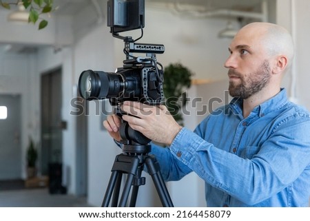 Videographer Filming with Video Camera on Film Set. Caucasian Camera Operator Holding Video Camera and Tripod with External Monitor