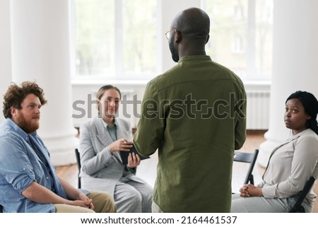 Rear view of young man sharing his trouble with patients attending psychological session or course of mental rehabilitation Royalty-Free Stock Photo #2164461537