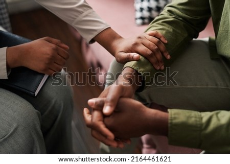 Young African American female psychologist keeping hand of wrist of male patient sitting in front of her and sharing his problems Royalty-Free Stock Photo #2164461621