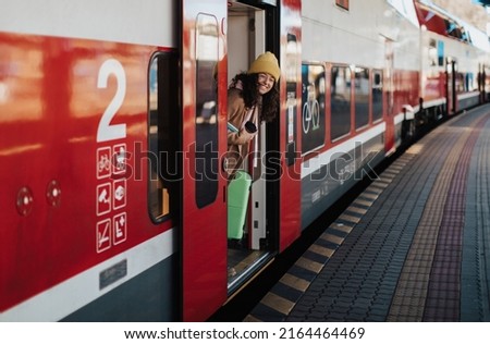Happy young traveler woman with luggage getting off the train at train station platform Royalty-Free Stock Photo #2164464469