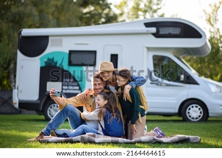 Happy young family with two children ltaking selfie with caravan at background outdoors.