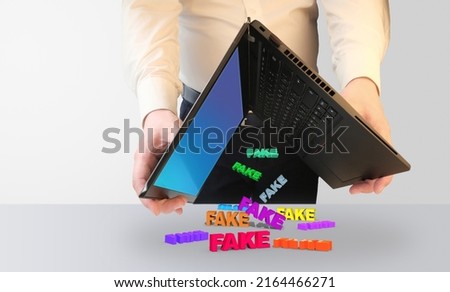 A man shakes a laptop from which words fall - fakes. layout with copy space. High quality photo