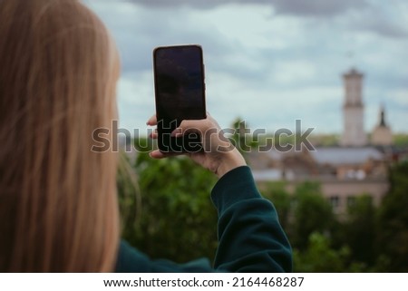 Closeup woman’s hand holding mobile phone taking photos of an old city in Europe. Female tourist or blogger enjoying trip. Travel and sightseeing concept