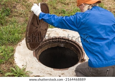 A working plumber opens a sewer hatch. Maintenance of septic tanks and water wells. selective focus Royalty-Free Stock Photo #2164468889
