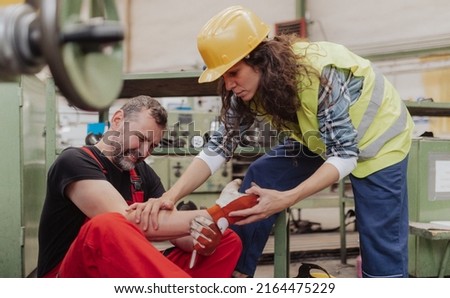 Woman is helping her colleague after accident in factory. First aid support on workplace concept. Royalty-Free Stock Photo #2164475229