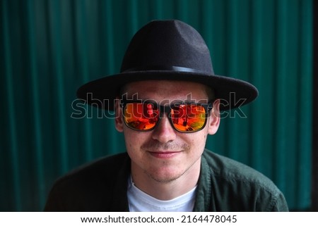 Smiling fashion man. Portrait of handsome smiling stylish hipster lambersexual model. Man dressed in red polarization sunglasses. Fashion male on the modern blue background. Face.