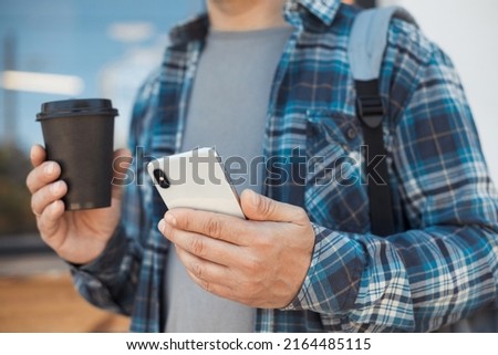 Urban faceless portrait of casual man using mobile phone and holding takeaway disposable coffee cup