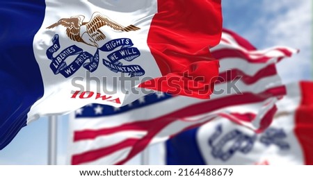 The Iowa state flag waving along with the national flag of the United States of America. In the background there is a clear sky. Iowa is a state in the Midwestern region of the United States Royalty-Free Stock Photo #2164488679
