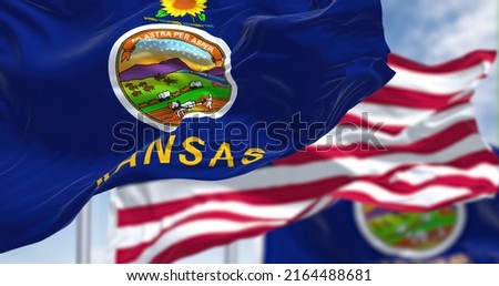 The Kansas state flag waving along with the national flag of the United States of America. In the background there is a clear sky. Kansas is a state in the Midwestern United States Royalty-Free Stock Photo #2164488681